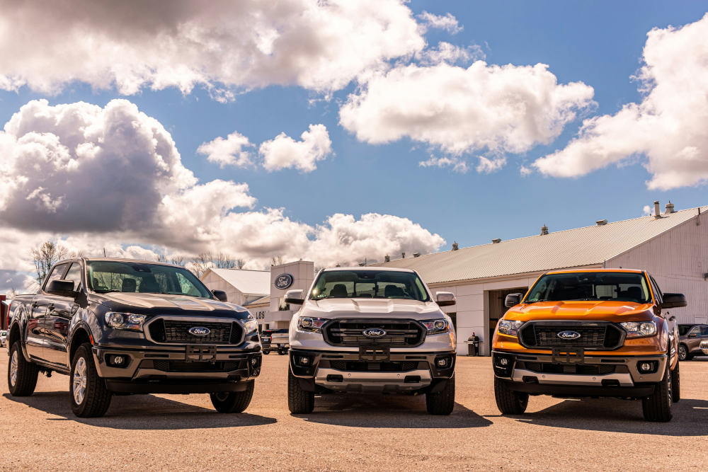A Ford Ranger is one of the top 3 vehicles target for car theft. there are 3 Ford rangers in a row, from left to right there is a black car, a silver car and a chevvy yellow one. 